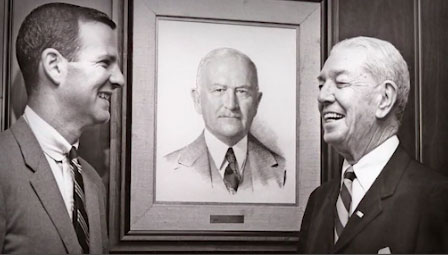Jim Baker standing with his father in front of a portrait of his grandfather